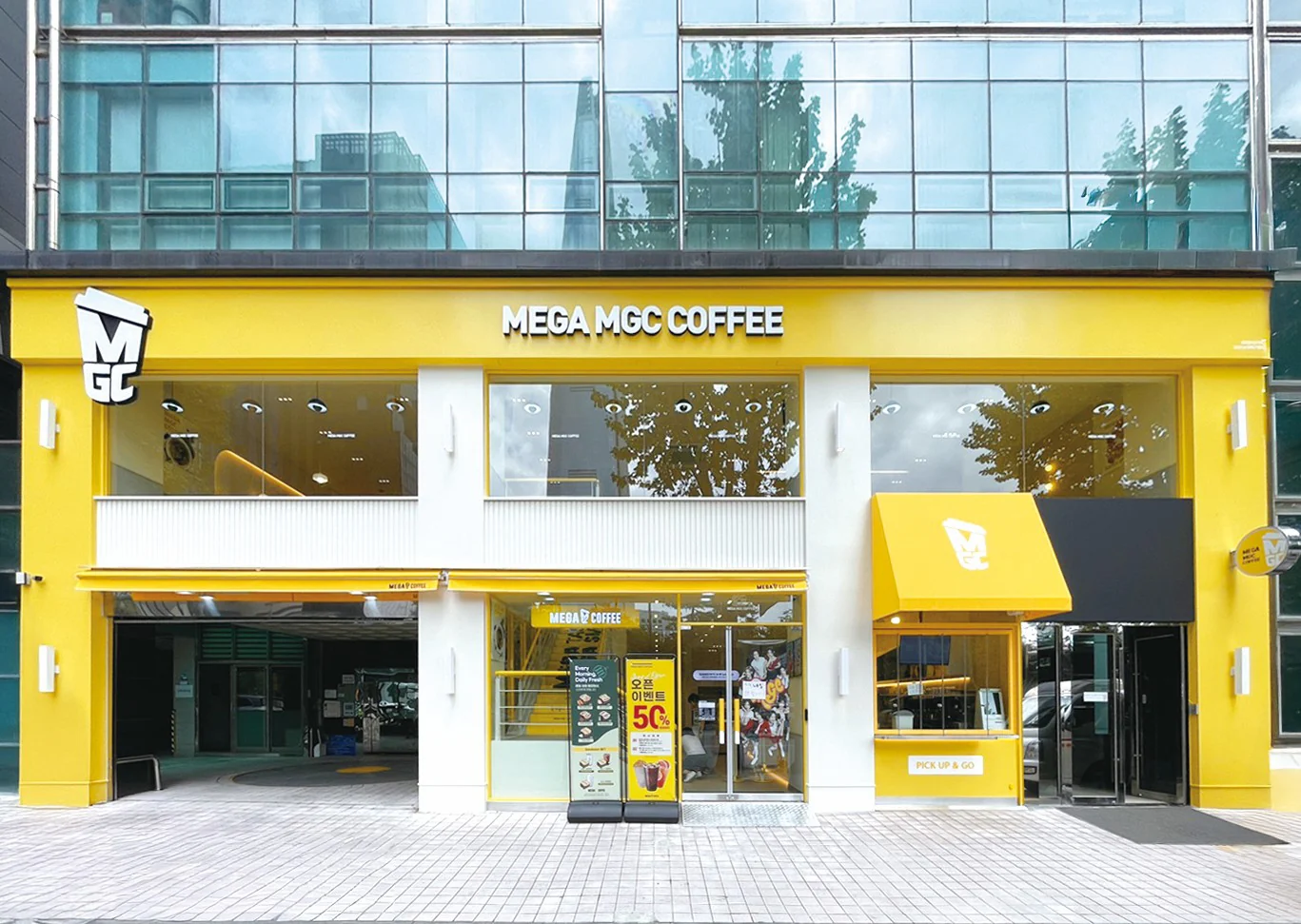 Bright yellow Mega MGC Coffee storefront with the brand sign above the entrance