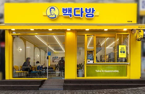 Yellow and navy Paik's Coffee storefront with Korean signage