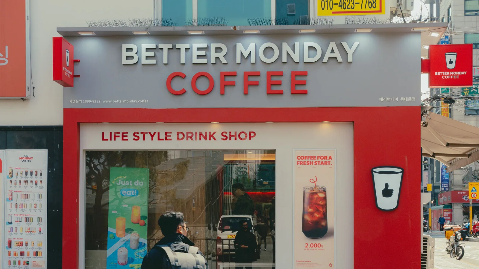 Pedestrian outside a compact Better Monday Coffee takeaway shop on a Seoul street