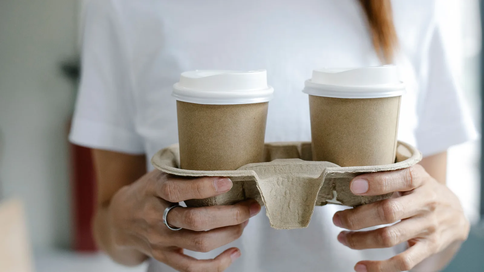 Person holding two takeaway coffee cups in a cardboard carrier