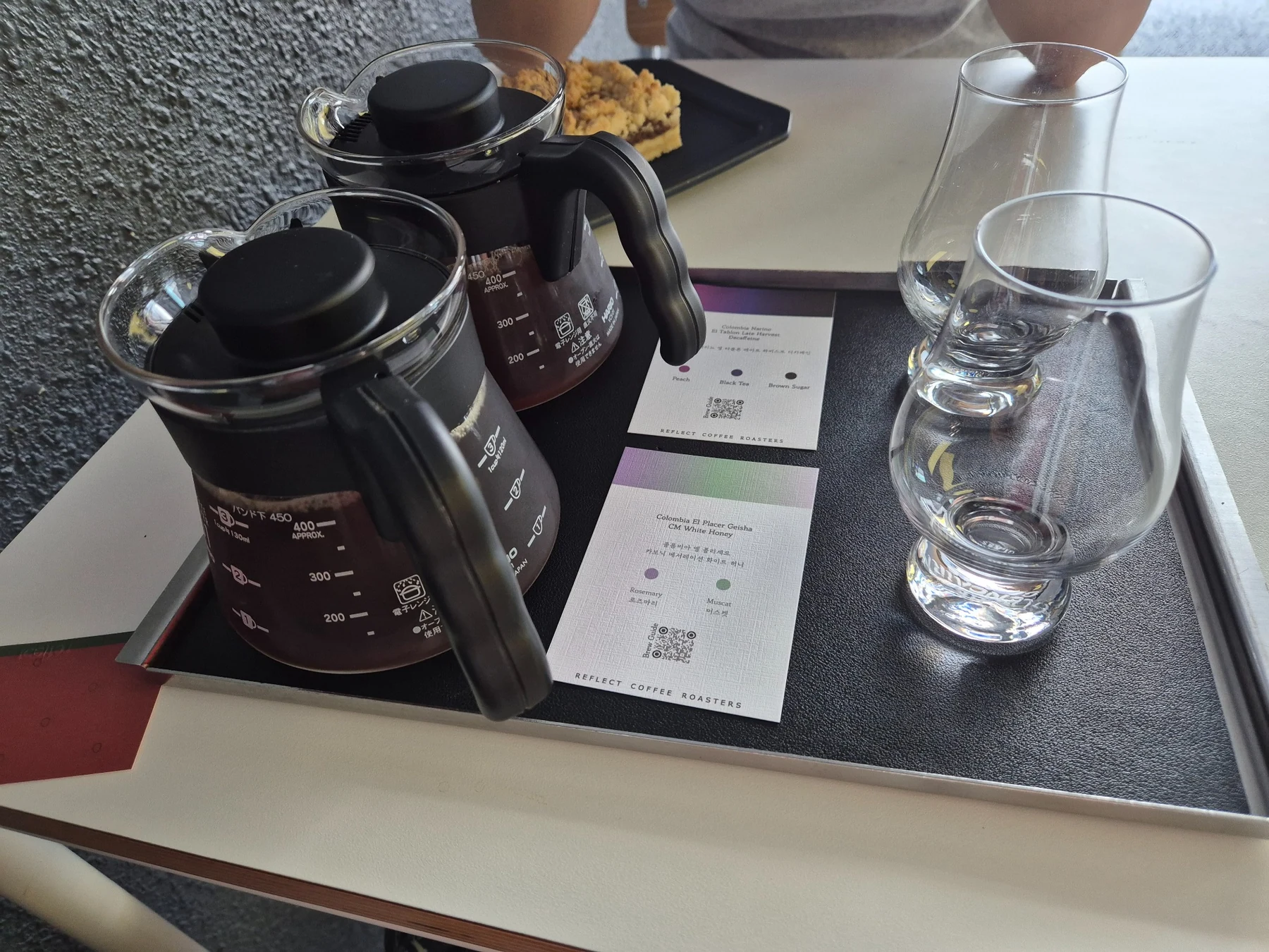 Two Reflect Coffee servers, tasting glasses and flavor cards on a black tray